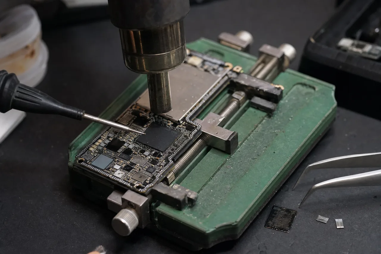A technician working on a circuit board at a microscope rework bench in the MDrepairs lab, the controlled environment where CPU, NAND and EEPROM packages are transplanted to a donor board